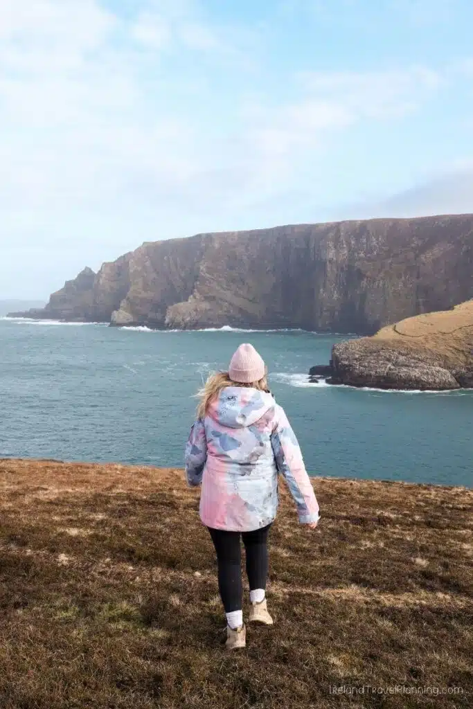 Woman in a floral jacket overlooking dramatic cliffs and the ocean in Ireland