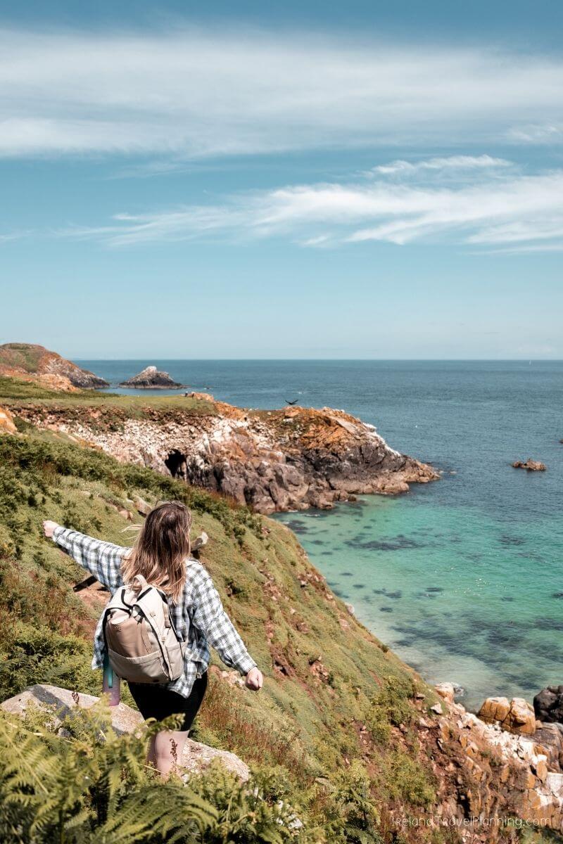 Woman hiking a coastal path in Ireland with turquoise sea