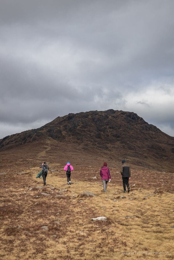 Four hikers walk towards a large mountain under a cloudy sky in Ireland.