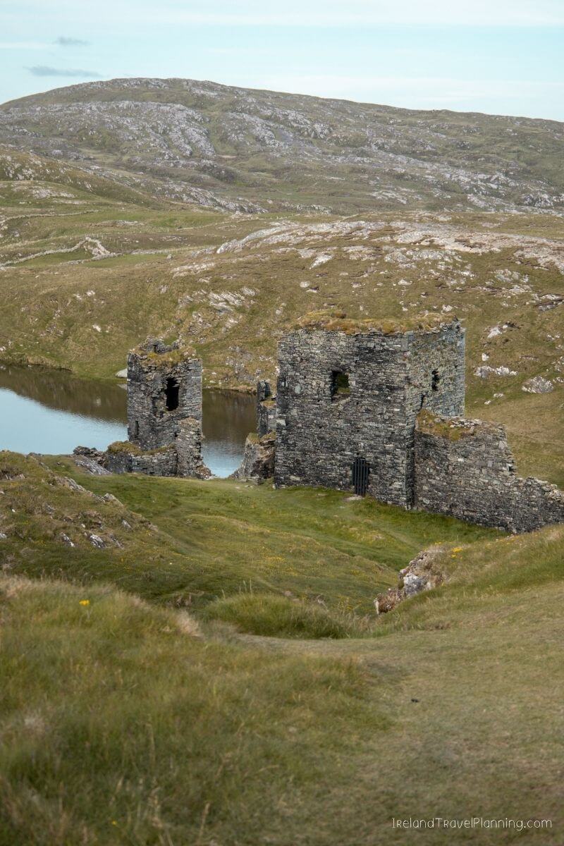 Ruins of a stone castle on a grassy hill overlooking a lake in Ireland
