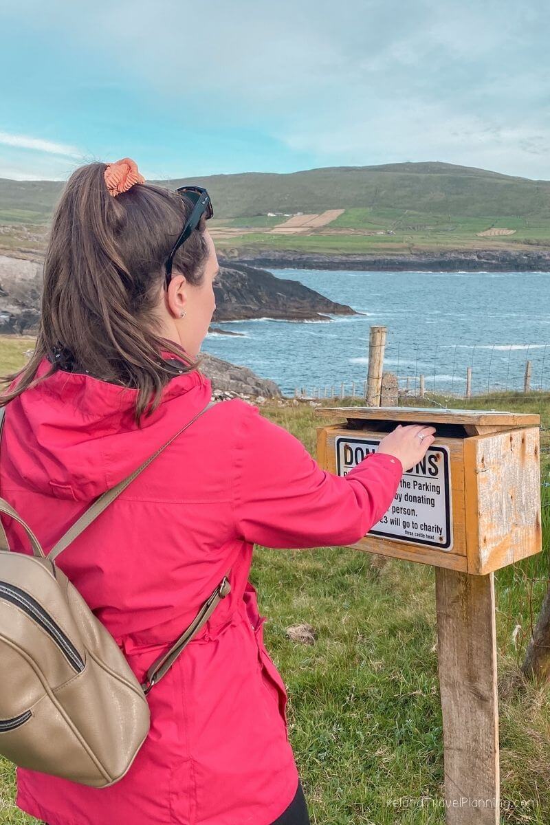 Woman donating to honesty box at scenic coastal viewpoint in Ireland