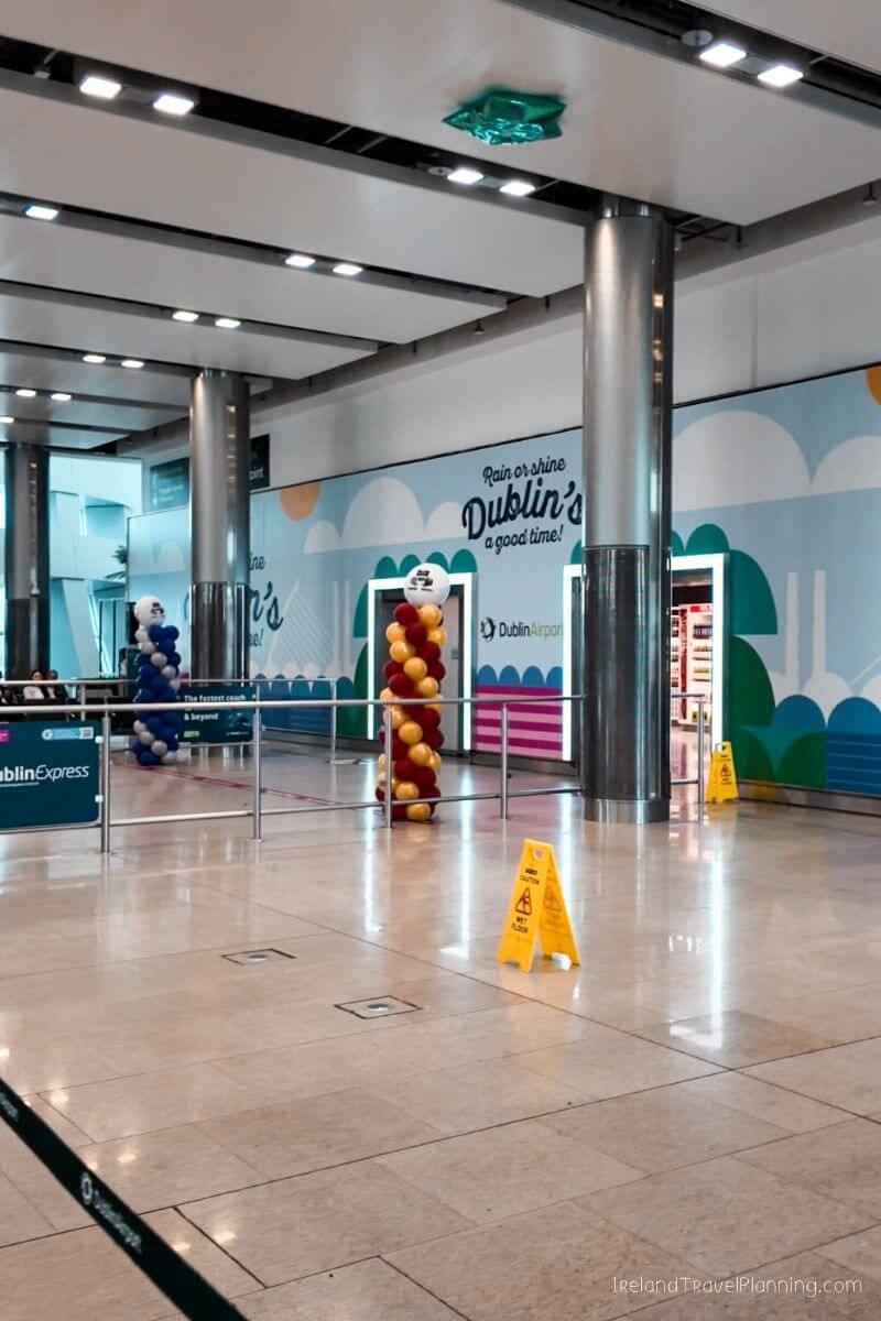 Dublin Airport arrivals hall with Dublin Express signage and wet floor signs.