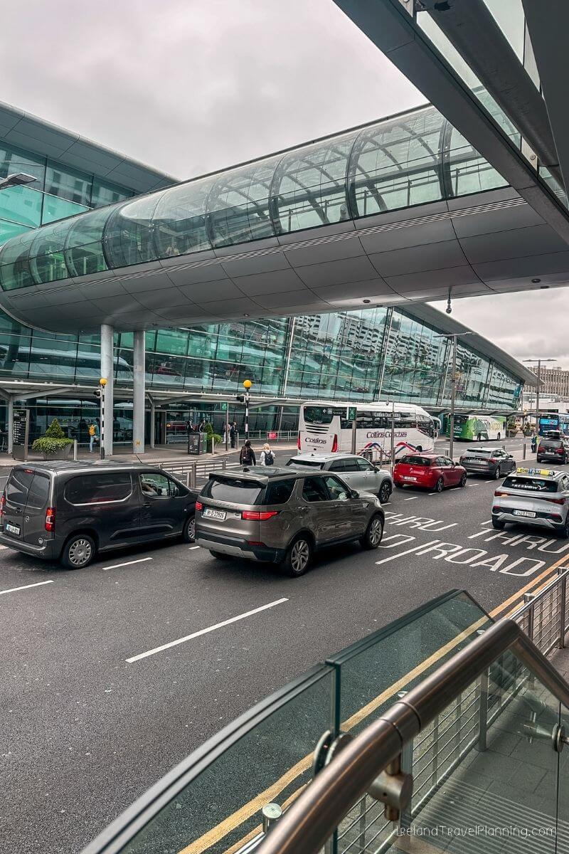 Cars and buses outside a modern airport terminal with a glass walkway.
