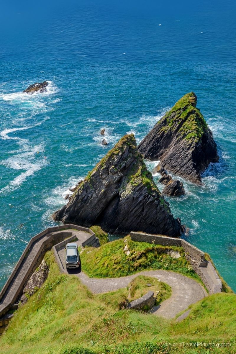 Car on winding road overlooking dramatic coastal cliffs and sea stacks in Ireland.