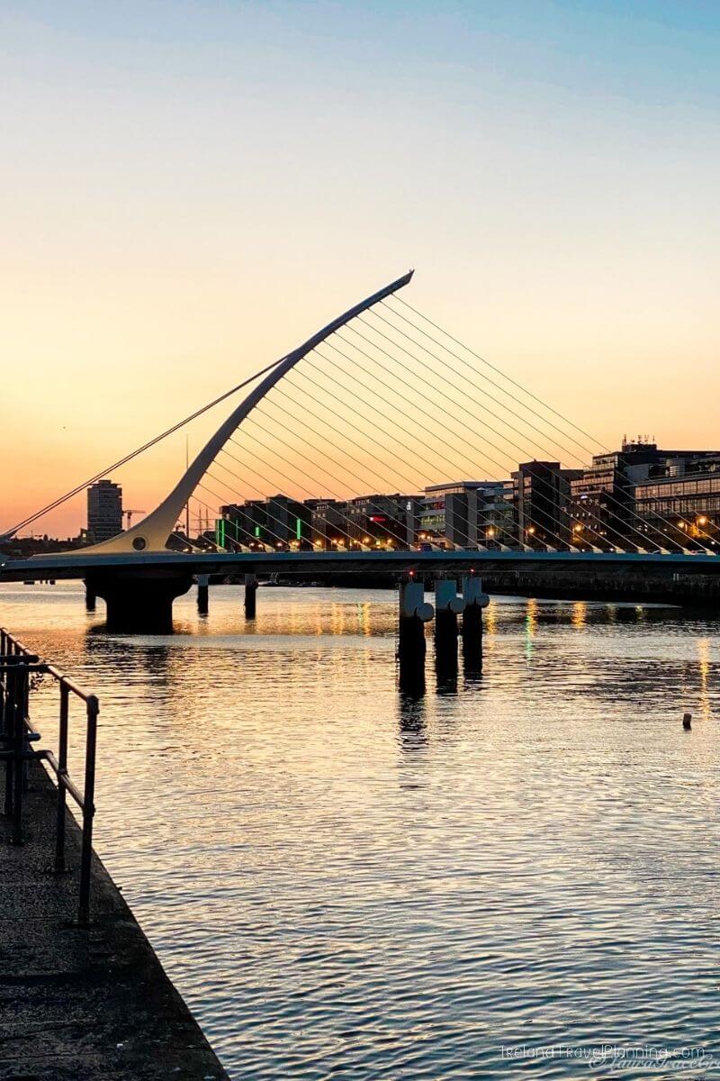 Samuel Beckett Bridge in Dublin at sunset with city lights reflecting on the River Liffey.