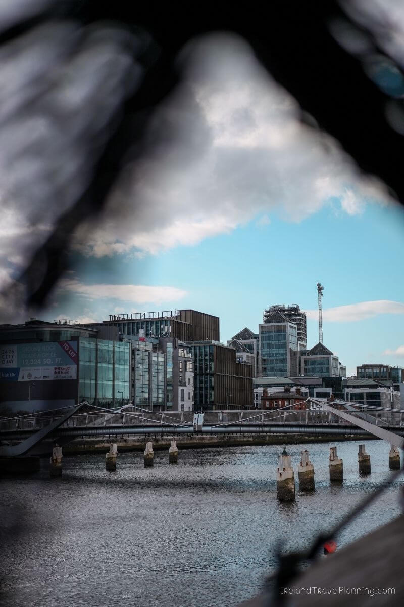 Modern Dublin cityscape with glass buildings and a river, framed by clouds.