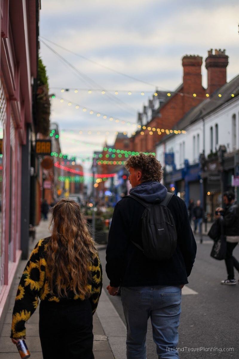 Couple walking down a street lined with shops and fairy lights in Ireland.