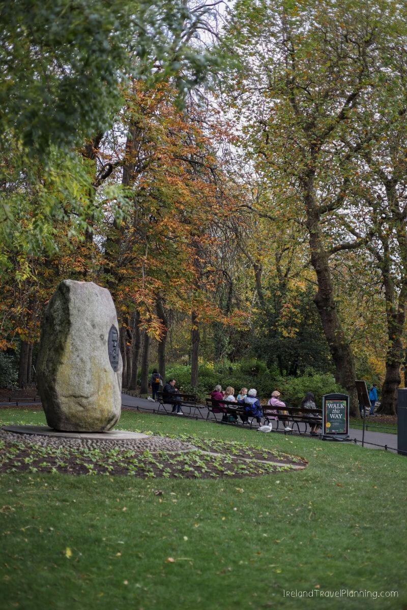 Autumn in St Stephen's Green Park, Dublin: People rest on benches near a large stone monument.