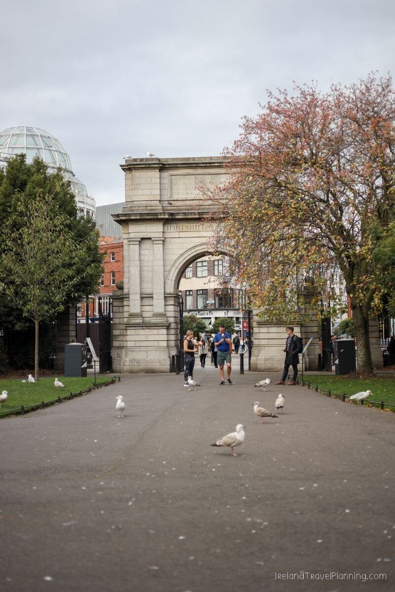 People walk through the Ha'penny Bridge archway in Dublin, with seagulls on the path.