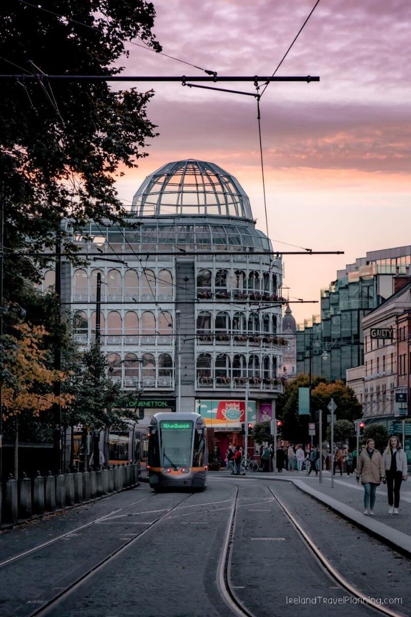 Dublin tram passes the historic General Post Office under a colorful sunset sky.