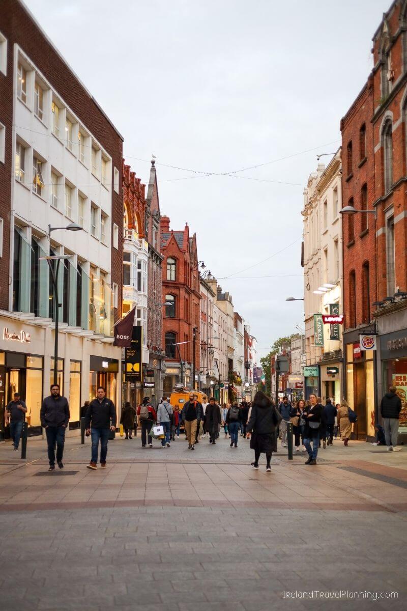 Crowded shopping street in Dublin, Ireland with people walking past shops.
