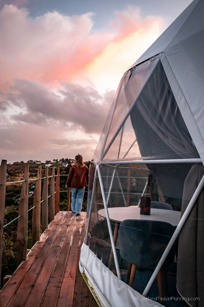 Woman on wooden walkway overlooking glamping dome with sunset sky