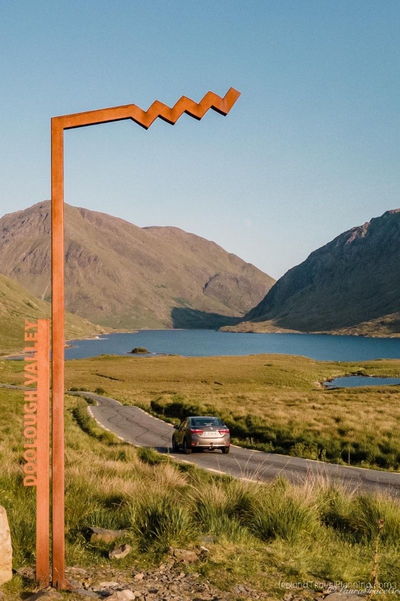 Doolough Valley signpost with car driving towards a lake in Ireland