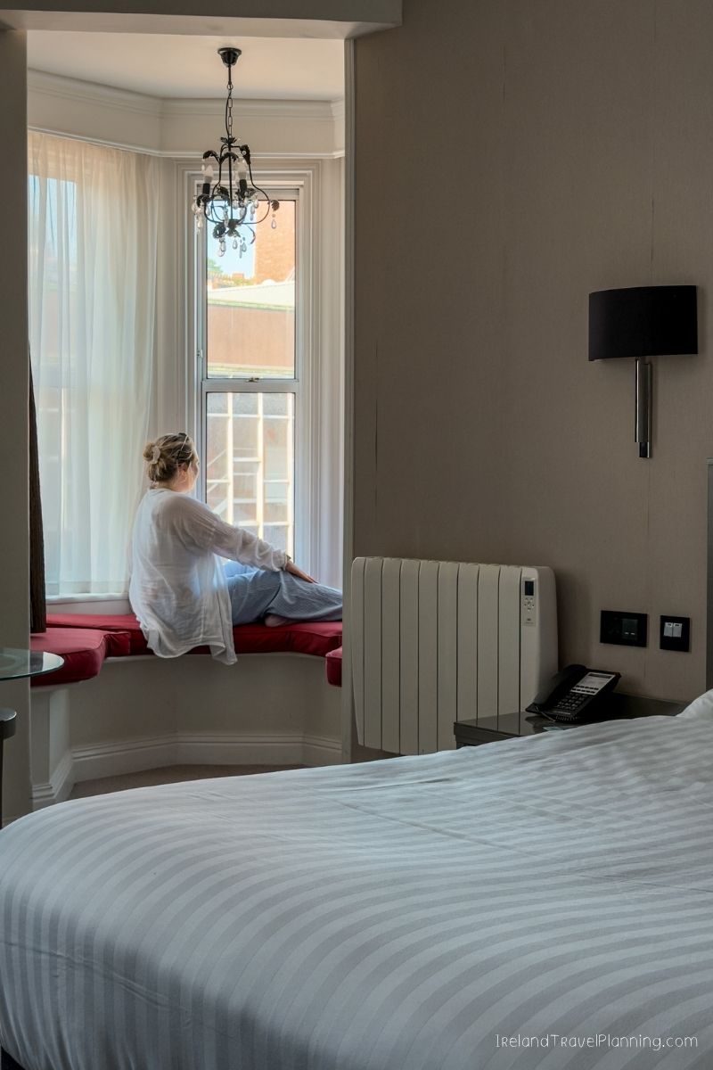 Woman looking out a bay window in an Irish hotel room, cost of Ireland trip