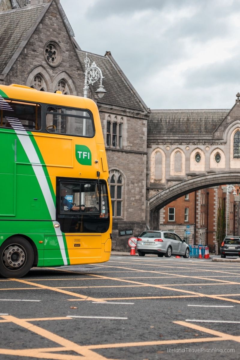 Yellow and green TFI bus in Dublin, Ireland, near historic architecture.