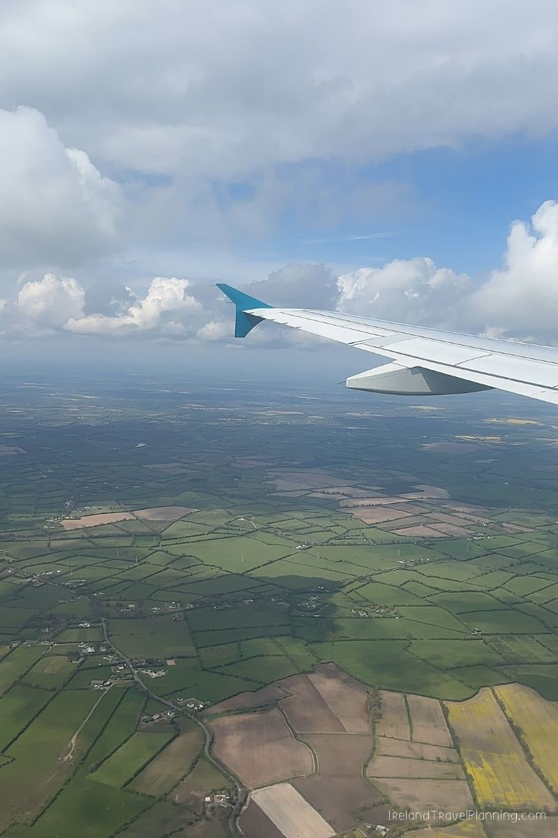 Airplane wing over green Irish countryside, hinting at Ireland trip costs.