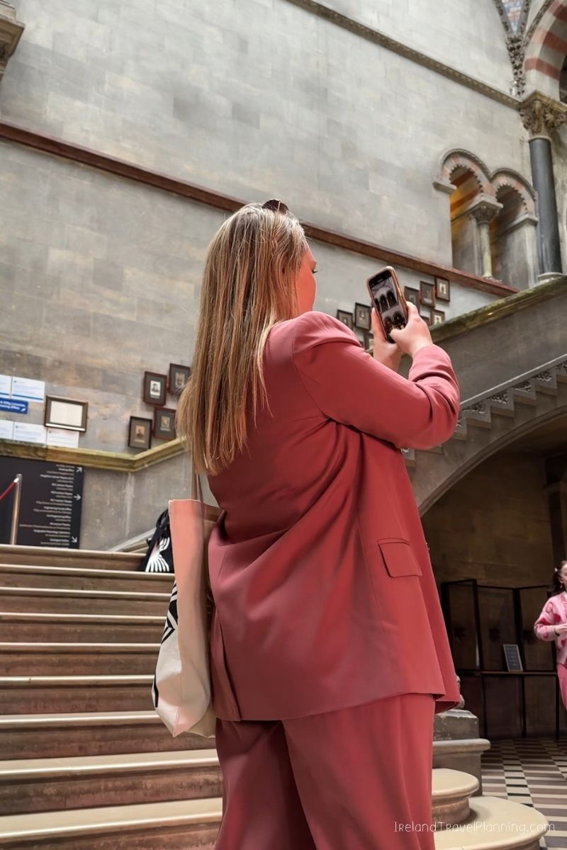 Woman in pink suit taking photo in grand staircase museum, Ireland travel