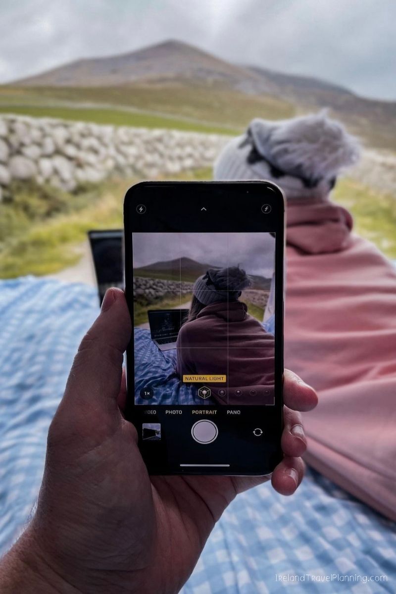 Couple on a picnic in Ireland, planning their trip cost on a laptop.