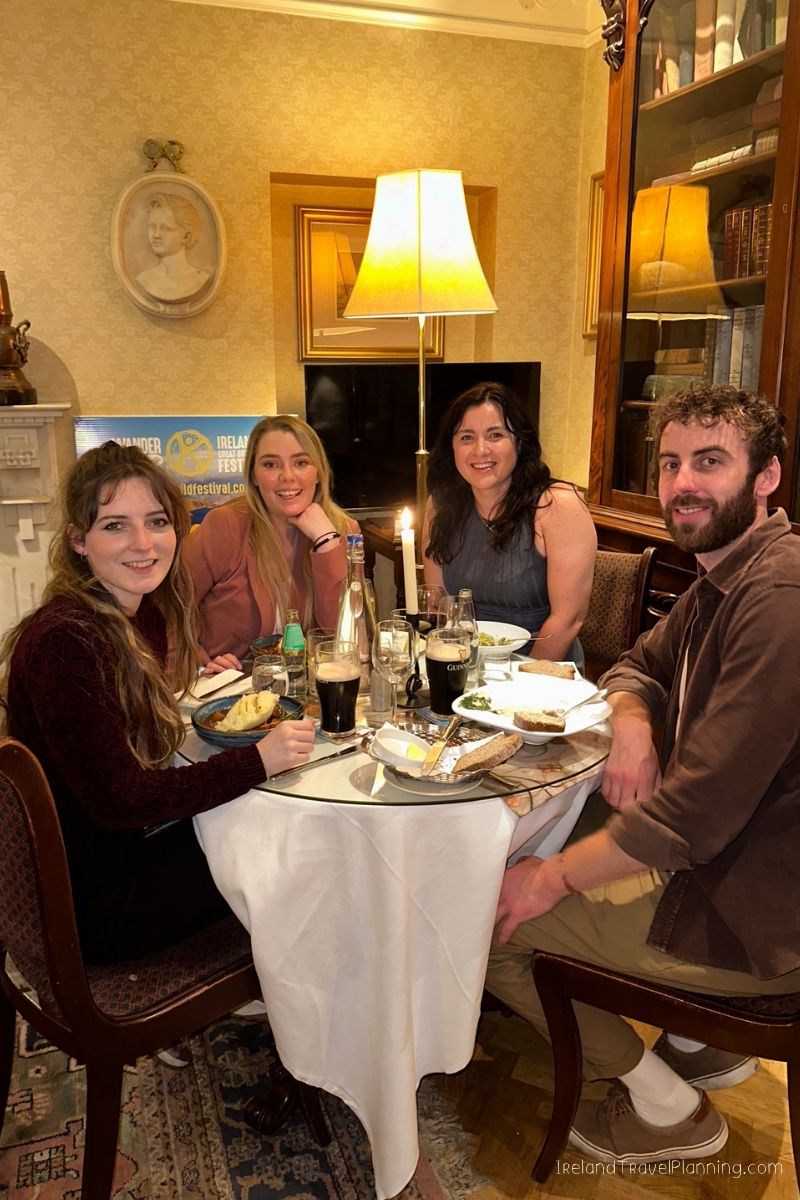 Four people enjoying dinner in an Irish pub, discussing Ireland trip costs.