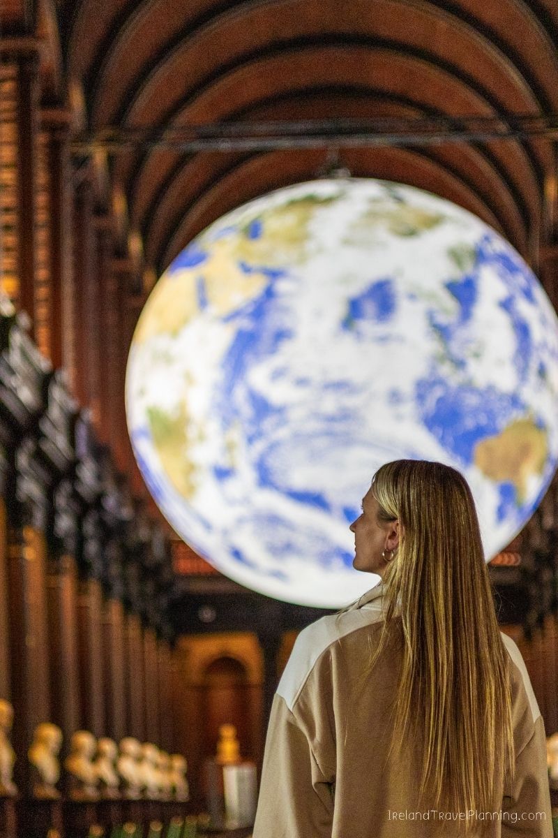 Woman looking at a large globe in a museum, Ireland trip cost context
