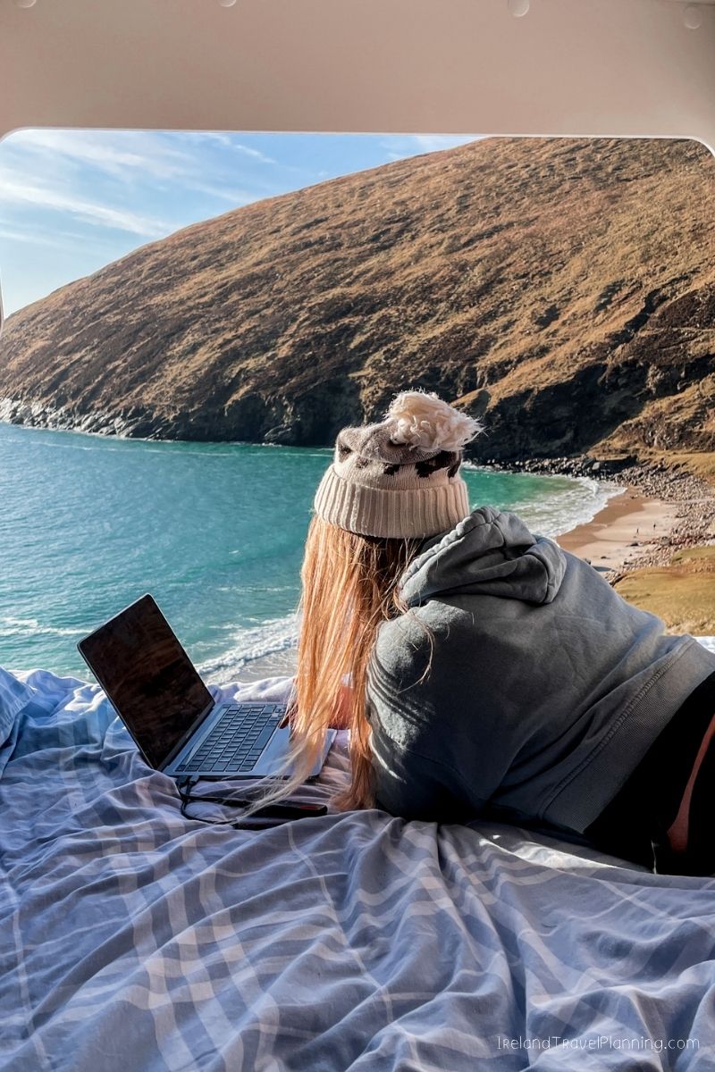 Woman working on a laptop with a stunning Irish coastal view