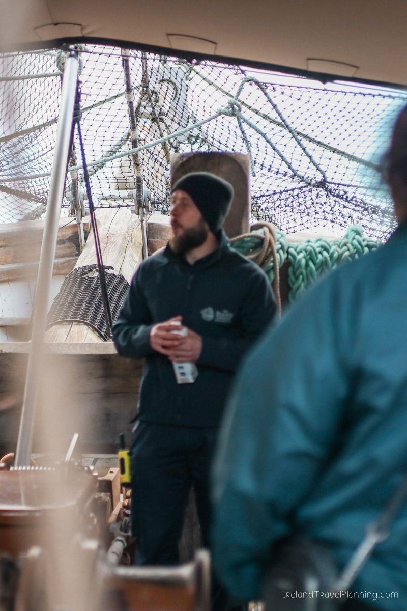 Man in beanie and dark jacket on a boat, possibly in Ireland.