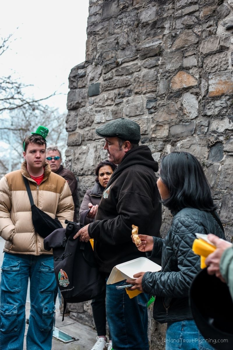 Tour group in Ireland, some holding food, near a stone wall