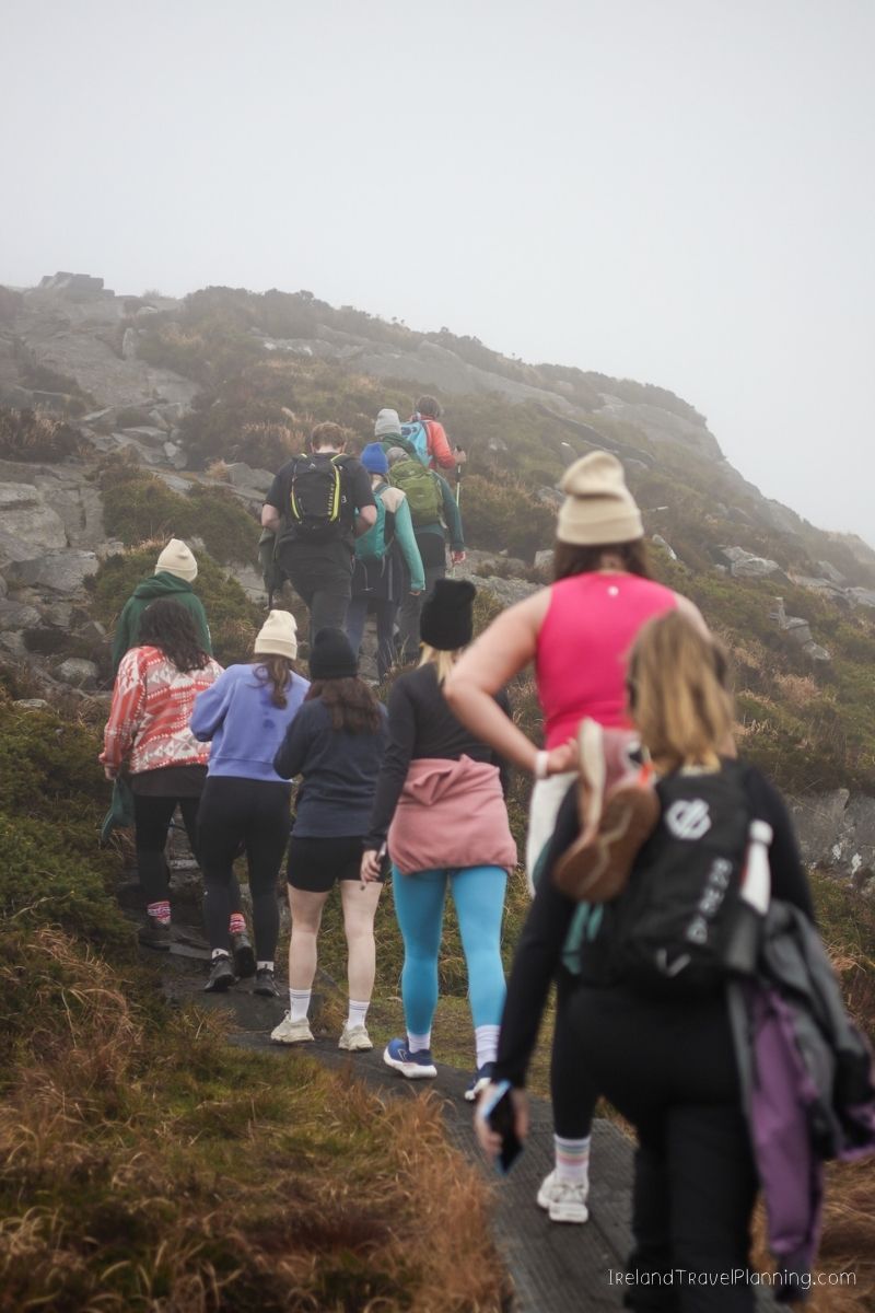 Hikers ascend a foggy mountain trail in Ireland, showcasing outdoor adventure costs.