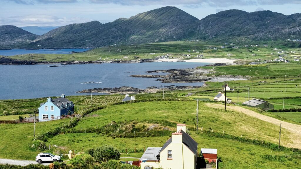 Green Irish countryside with blue bay, mountains, and houses. Ideal for a trip.