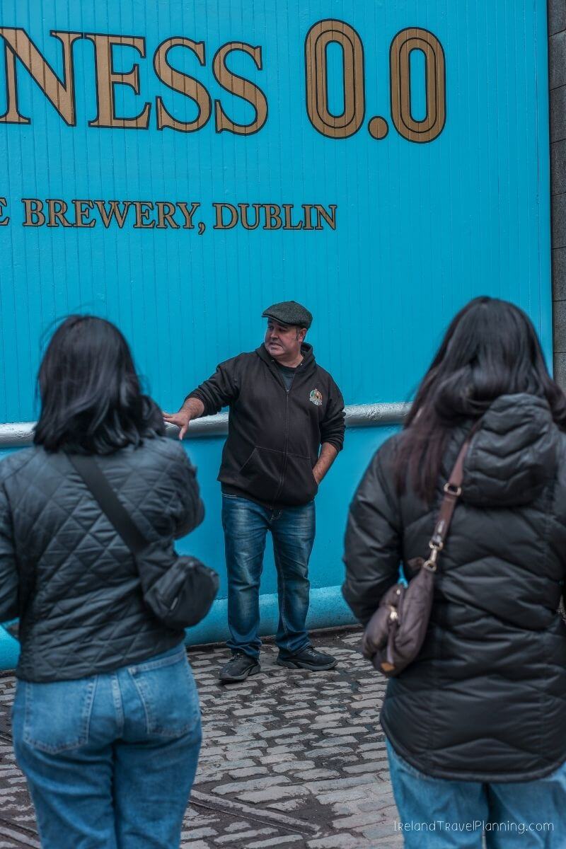 Guinness 0.0 Brewery, Dublin: Man in flat cap speaks to two women.
