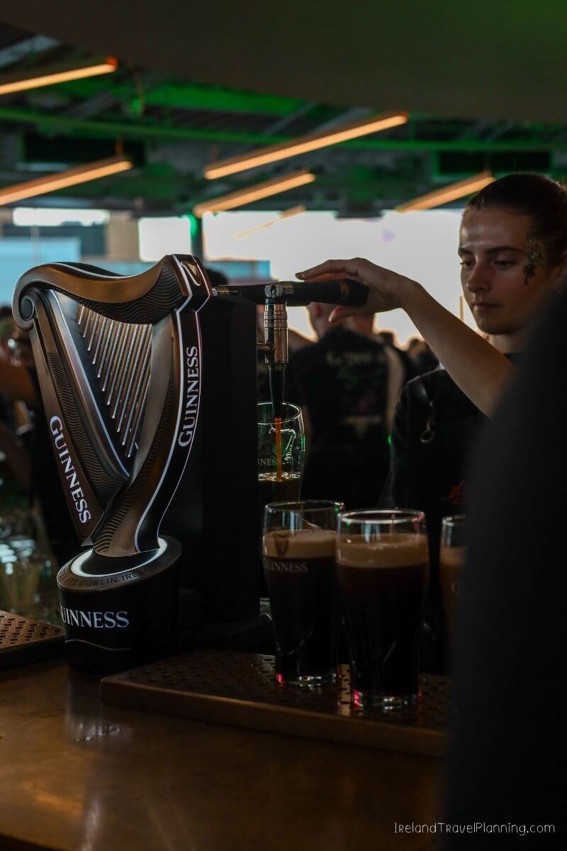 Bartender pouring Guinness beer from a tap into glasses in a bar.