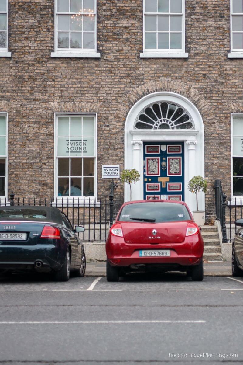 Red Renault Clio parked outside a brick building with arched doorway and "AVISON YOUNG" signs.