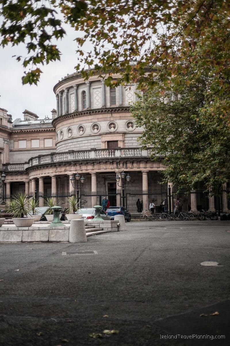The National Library of Ireland, a grand building with columns and a curved facade, seen through autumn leaves.