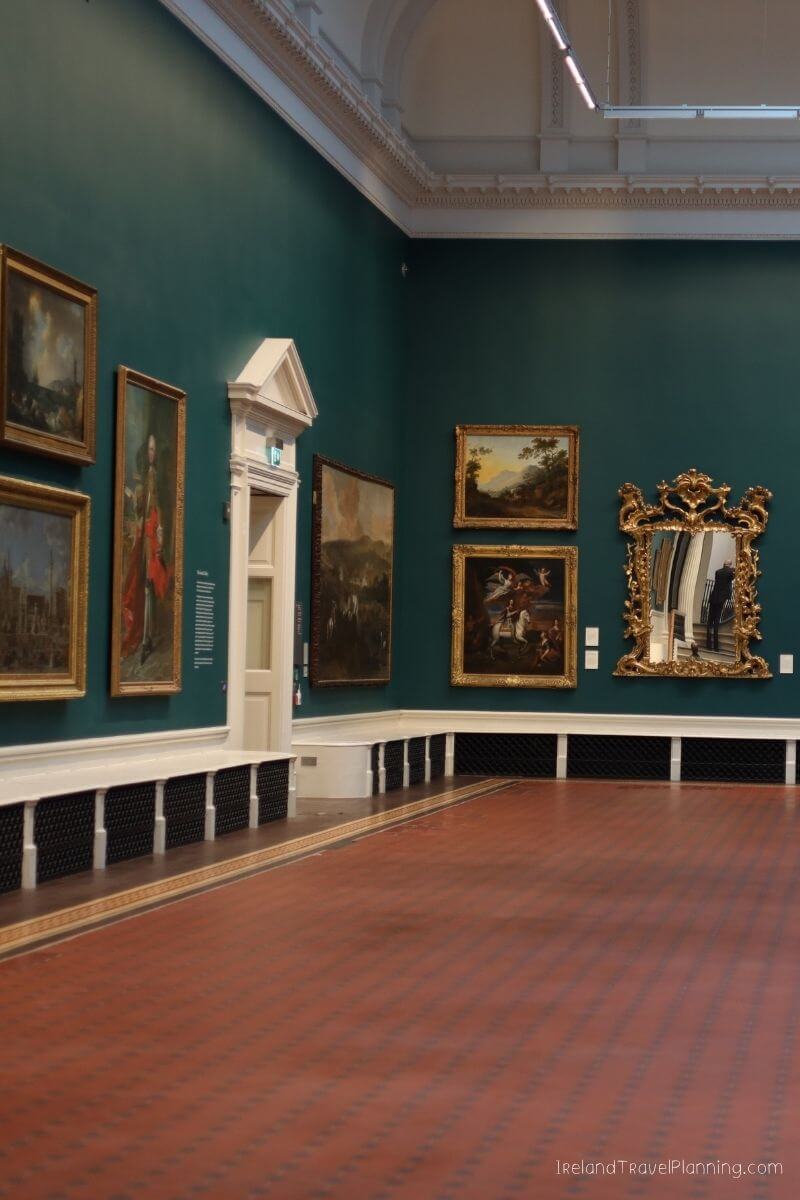 Art gallery with paintings on teal walls, ornate mirror, and red tiled floor