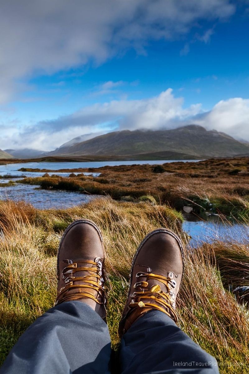 Hiking boots resting on grassy terrain with a scenic Irish landscape in the background.
