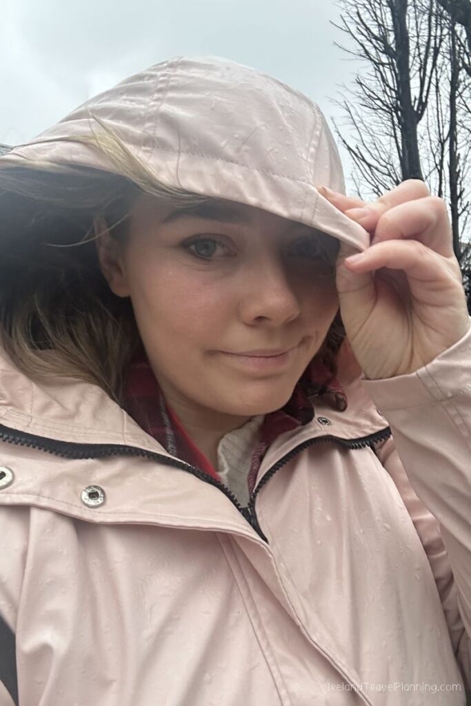 Woman in pink raincoat and hood, holding hood down in light rain, Ireland Travel Planning