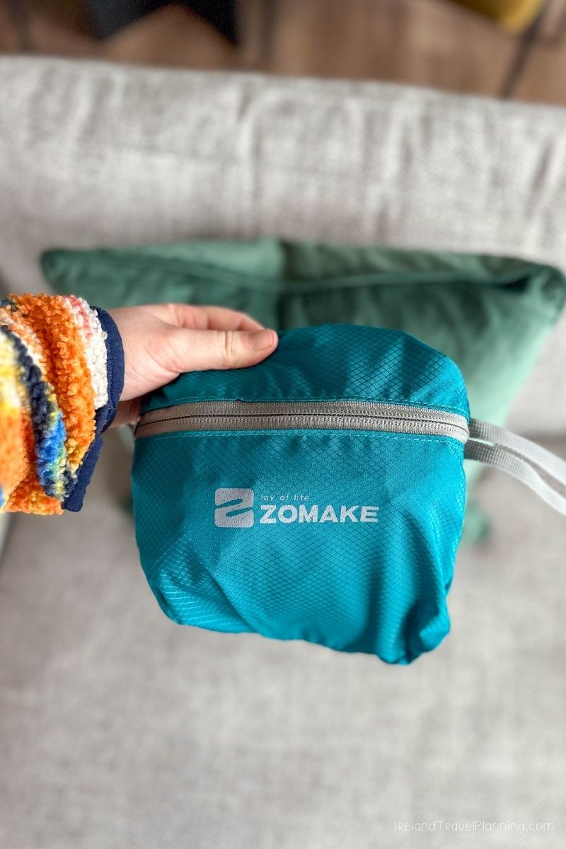 Teal ZOMAKE travel pouch held by a hand with a colorful sleeve
