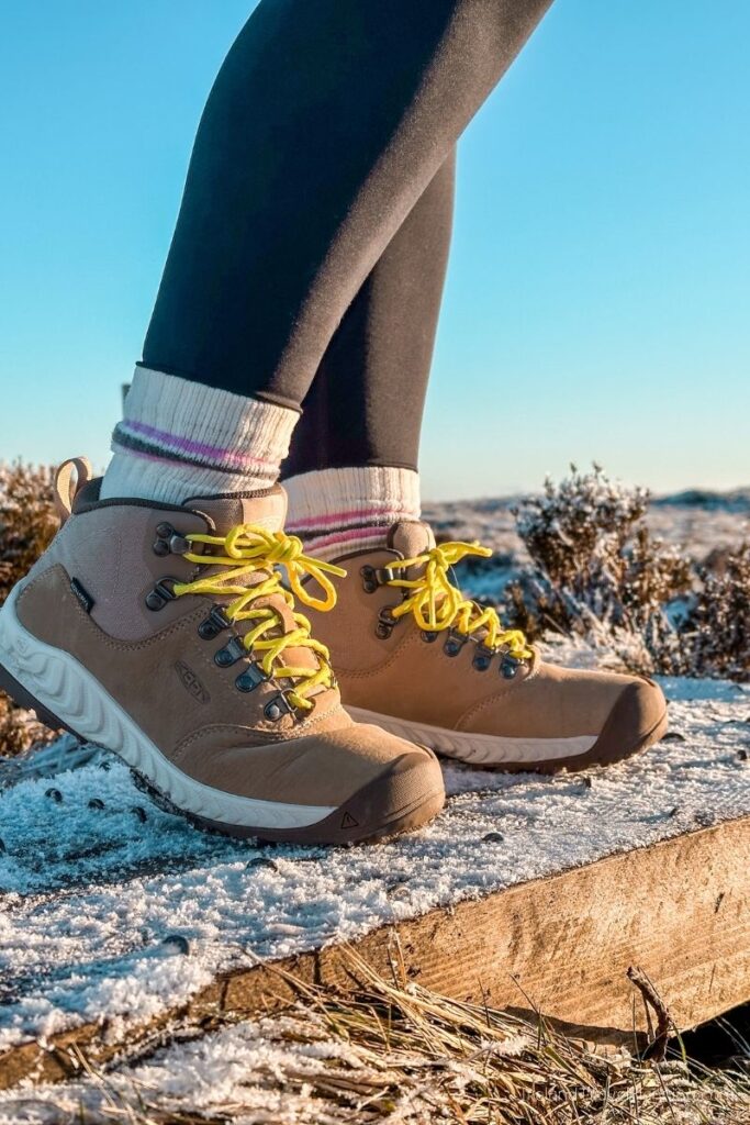 Woman wearing tan Keen hiking boots with yellow laces on a frosty trail.