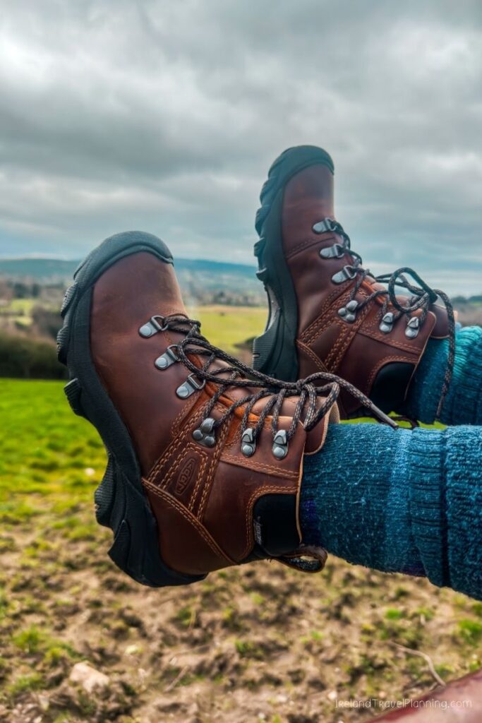 Brown leather Keen hiking boots laced up, worn with blue wool socks, outdoors.