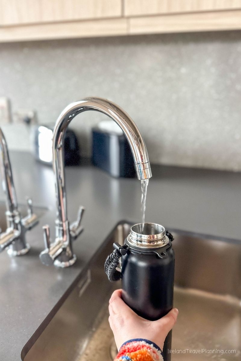Hand filling a black reusable water bottle from a kitchen faucet
