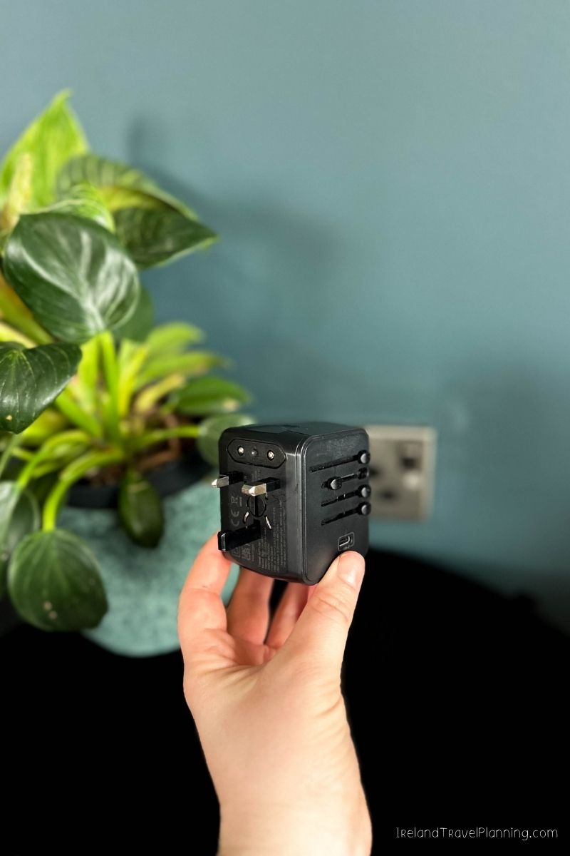 Hand holding a black universal travel adapter with world plug adapters