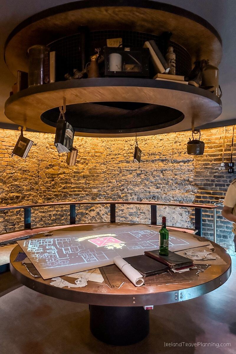 Round table with projected map, books, and bottle in a room with brick walls.