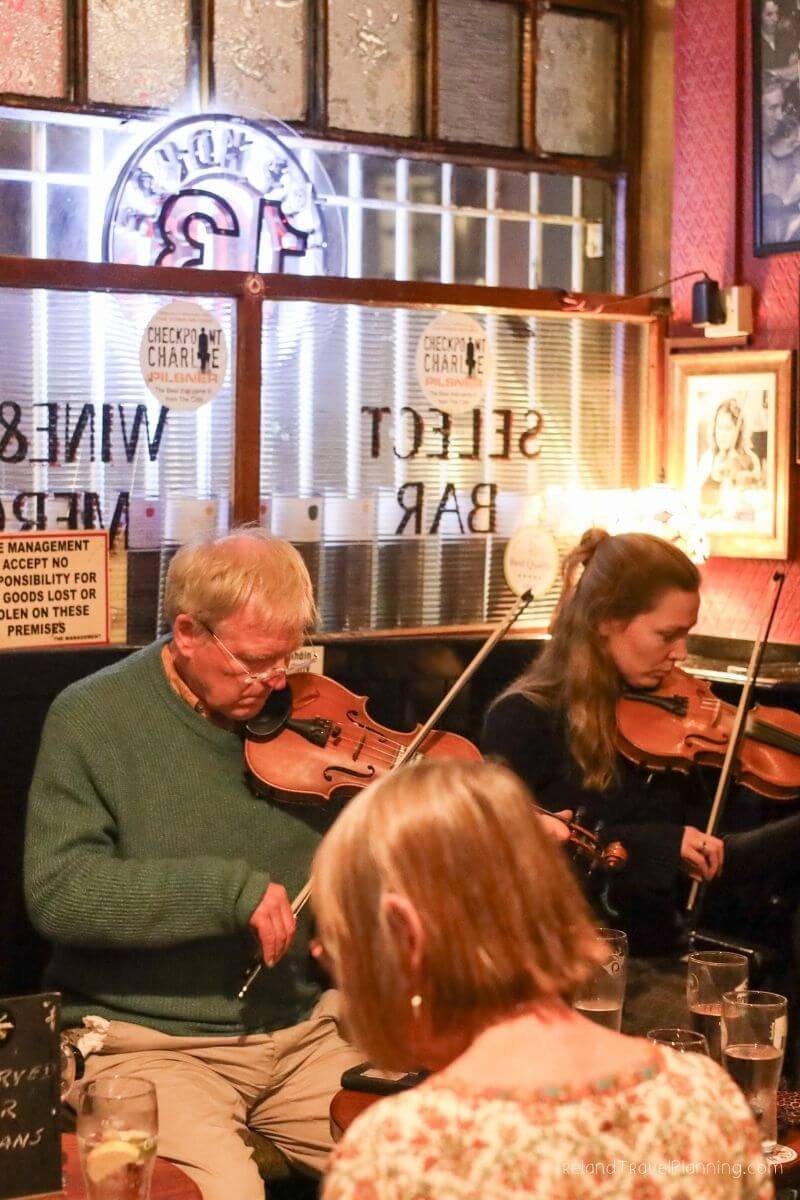 Musicians play violins in a dimly lit pub with neon signs