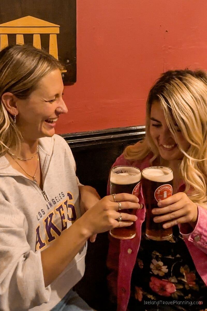 Two laughing women clinking glasses of Smithwick's beer in an Irish pub