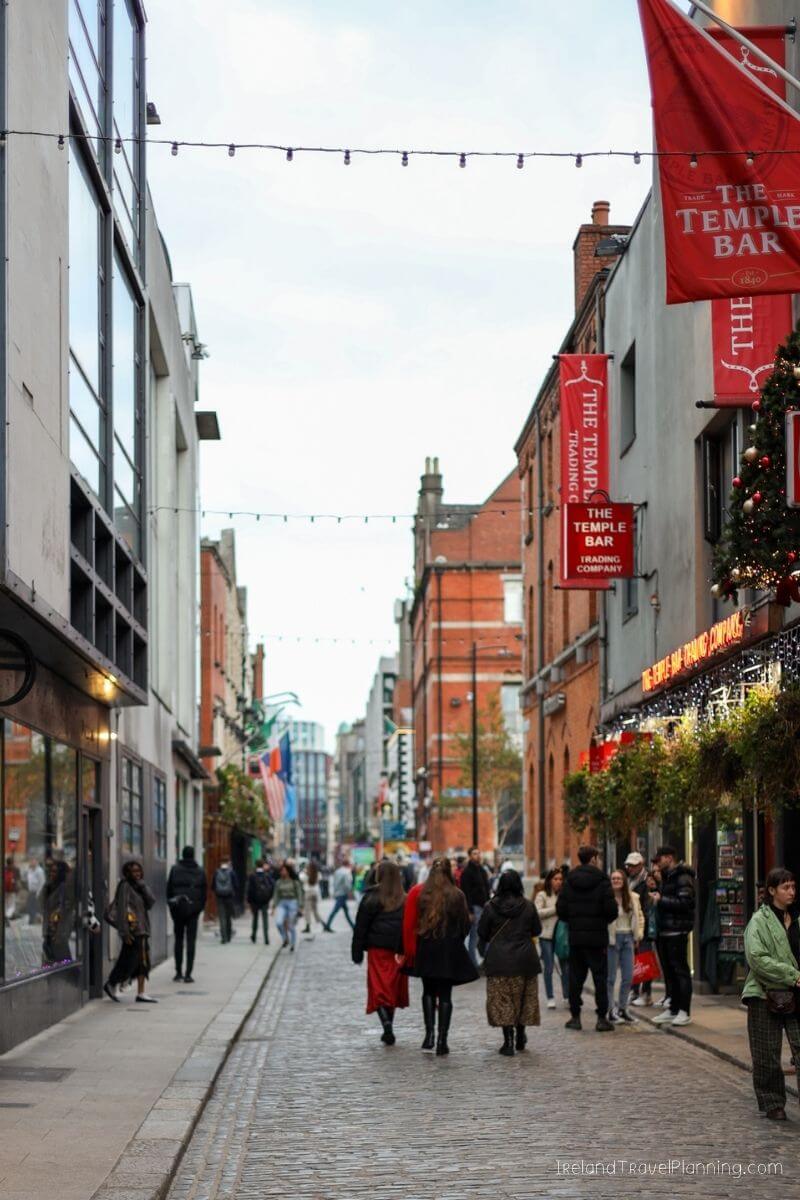 People walk down a cobblestone street in Dublin, Ireland, with The Temple Bar visible.